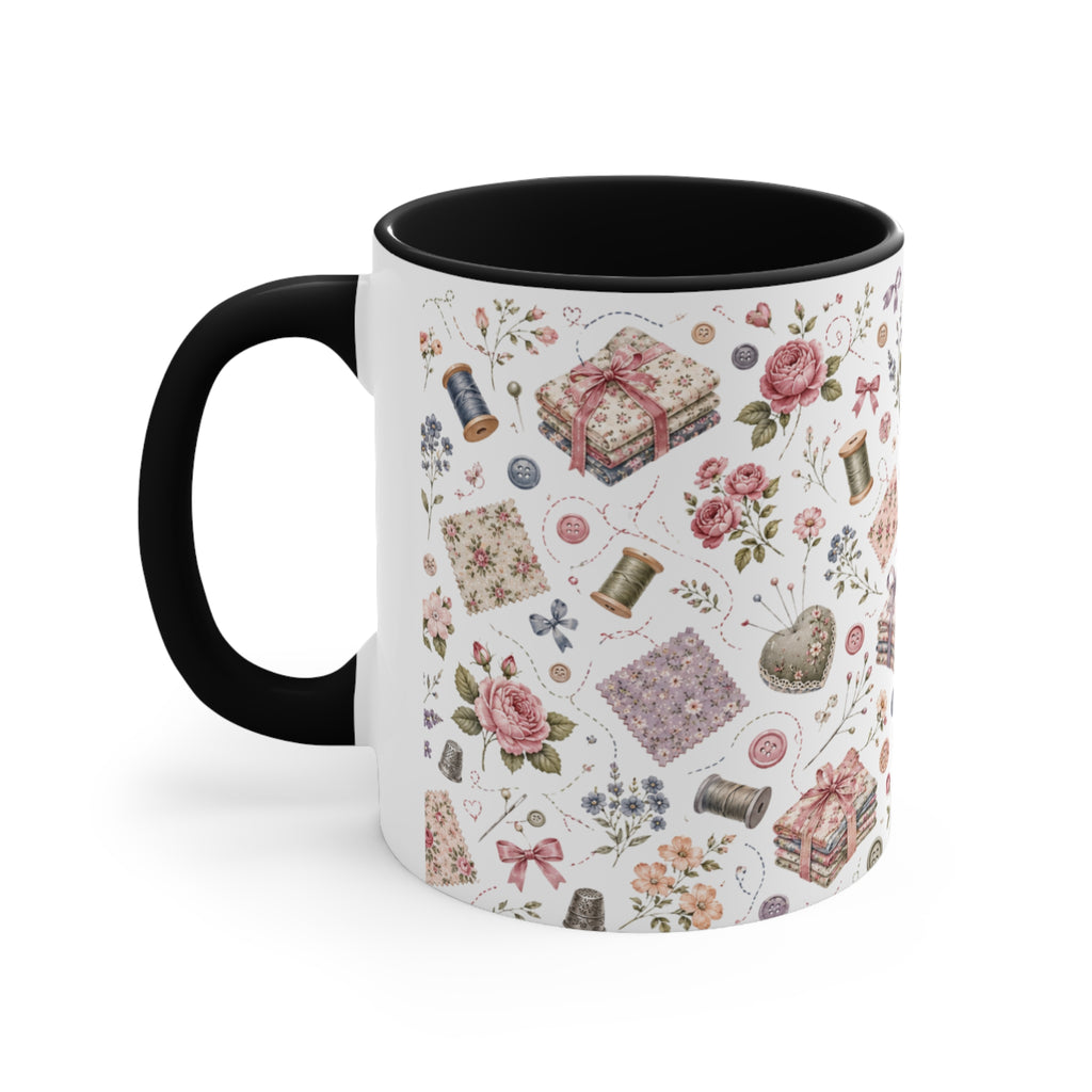 A white ceramic mug with a black interior, decorated with a vintage-style sewing and crafting pattern featuring pink roses, thread spools and fabric. The handle is on the left.