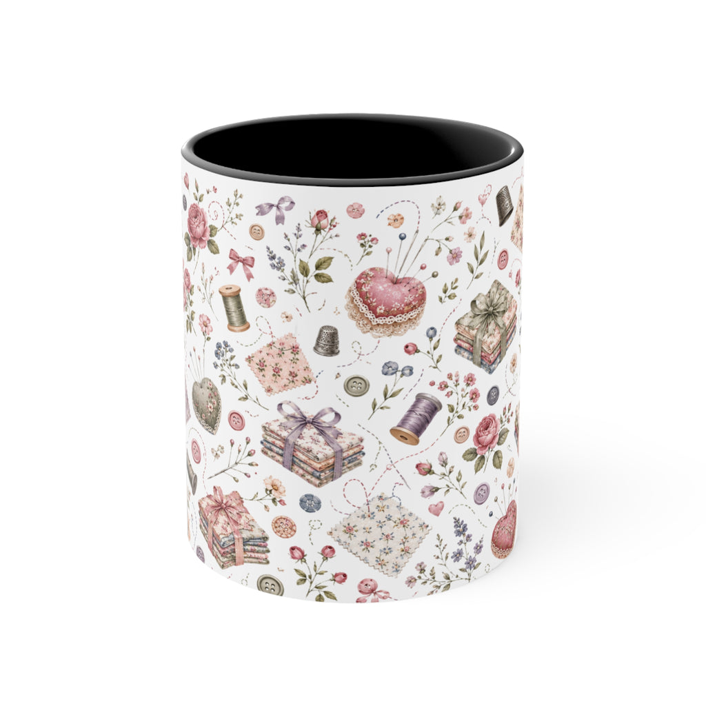 A white ceramic mug with a black interior, decorated with a vintage-style sewing and crafting pattern featuring pink roses, thread spools and fabric. The handle is not visible.