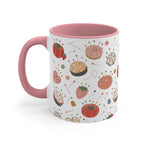 A ceramic mug with a white exterior decorated with a colorful pattern of pumpkins, tomatoes, and sewing pins, featuring a solid pink handle and interior, set against a plain white background.