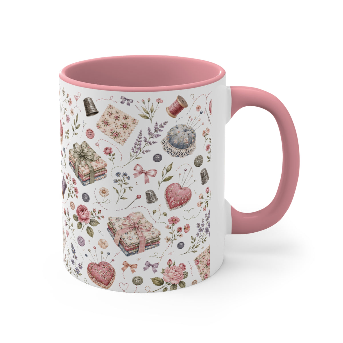 A white ceramic mug with a pink interior and handle, decorated with a vintage-style pattern of sewing notions, flowers, and hearts in muted pink, beige, and blue tones. The handle is on the right.
