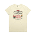 A light butter yellow short-sleeve crewneck t-shirt with a festive Christmas graphic on the front. The graphic features the text 'ALL I WANT FOR CHRISTMAS IS MORE FABRIC' in a mix of black and red fonts, surrounded by illustrations of a ribbon-tied fabric stack, a thread spool, and holly leaves.