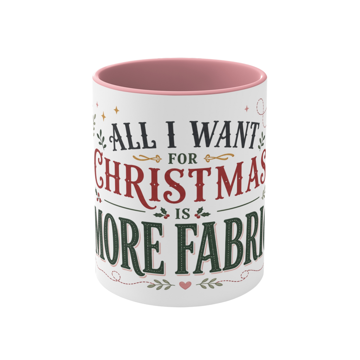 The front of a white ceramic mug with a pink interior and rim, showing the words "All I Want for Christmas is More Fabric'. The text is styled in dark green and red fonts with small holly and heart accents.