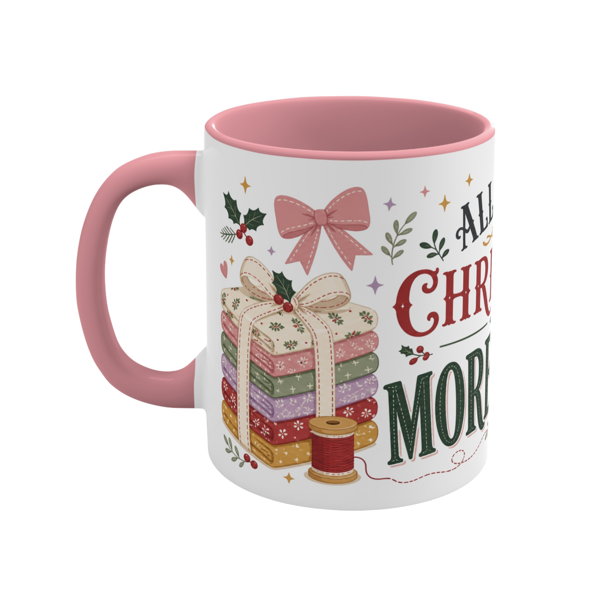 The left side of a white ceramic mug with a pink handle and interior, decorated with a bundle of fabric, a pink ribbon, thread spool and holly. The text 'All I Want for Christmas is More Fabric' is partially visible.
