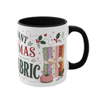 The right side of a white ceramic mug with a black handle and interior, decorated with a bundle of fabric, a pincushion and holly. The text 'All I Want for Christmas is More Fabric' is partially visible.