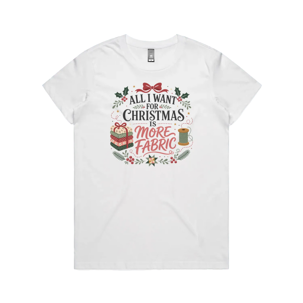 A white short-sleeve crewneck t-shirt with a festive Christmas graphic on the front. The graphic features the text 'ALL I WANT FOR CHRISTMAS IS MORE FABRIC' in a mix of black and red fonts, surrounded by illustrations of a ribbon-tied fabric stack, a thread spool, and holly leaves.