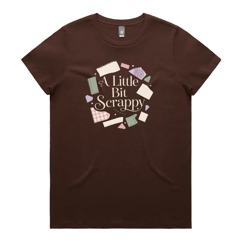 A dark brown short-sleeve crewneck t-shirt featuring a circular graphic on the chest with the text 'A Little Bit Scrappy' surrounded by small colorful fabric pieces.