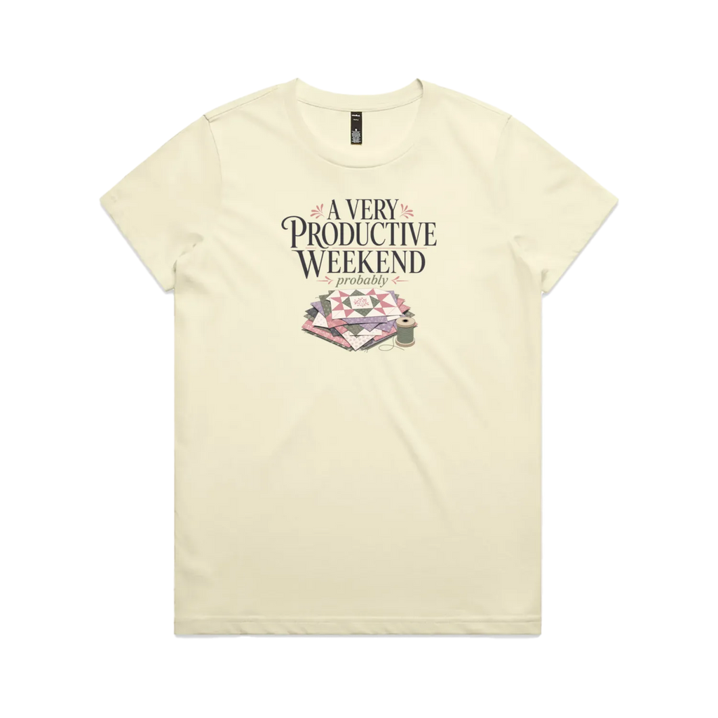 A pale butter yellow short-sleeve graphic t-shirt featuring the words 'A Very Productive Weekend, probably' above a stack of patchwork blocks and a thread spool.