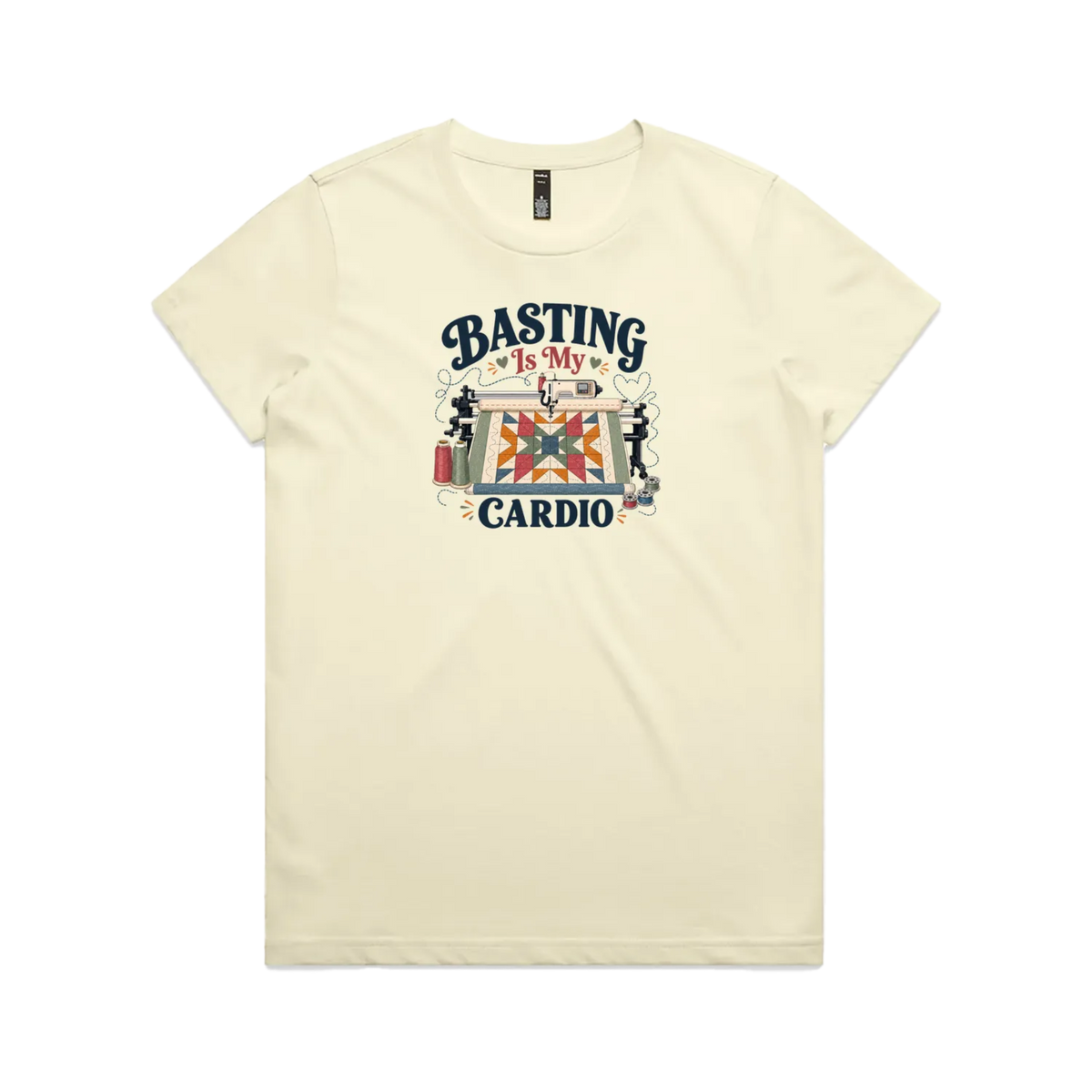 A pale butter yellow short-sleeve t-shirt featuring the words 'Basting Is My Cardio' with an illustration of a longarm quilting machine, a quilt and thread.
