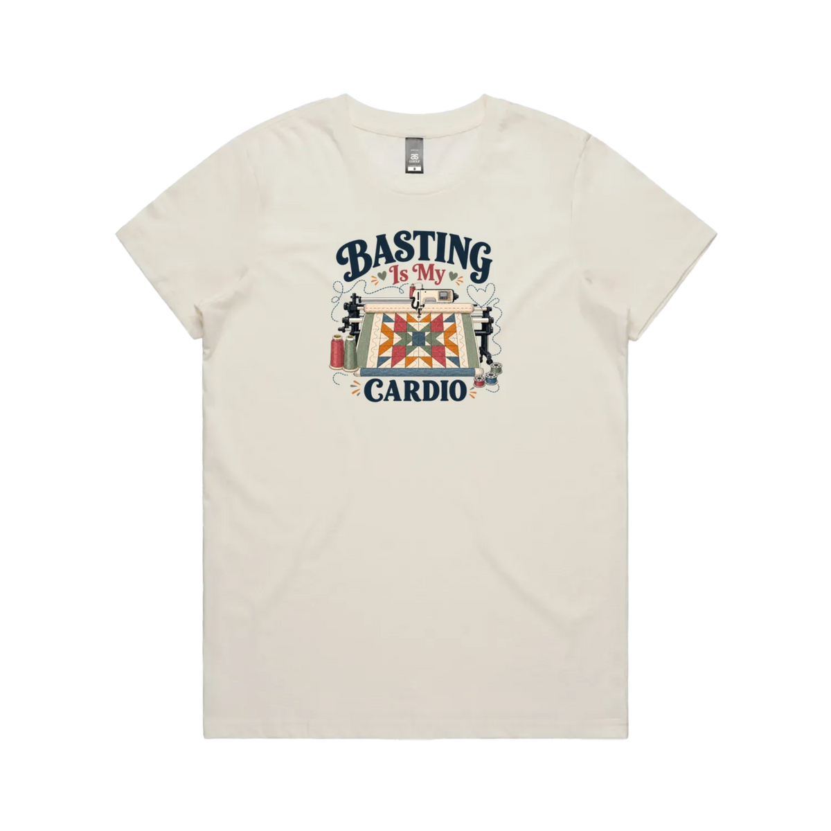 An off-white short-sleeve t-shirt featuring the words 'Basting Is My Cardio' with an illustration of a longarm quilting machine, a quilt and thread.