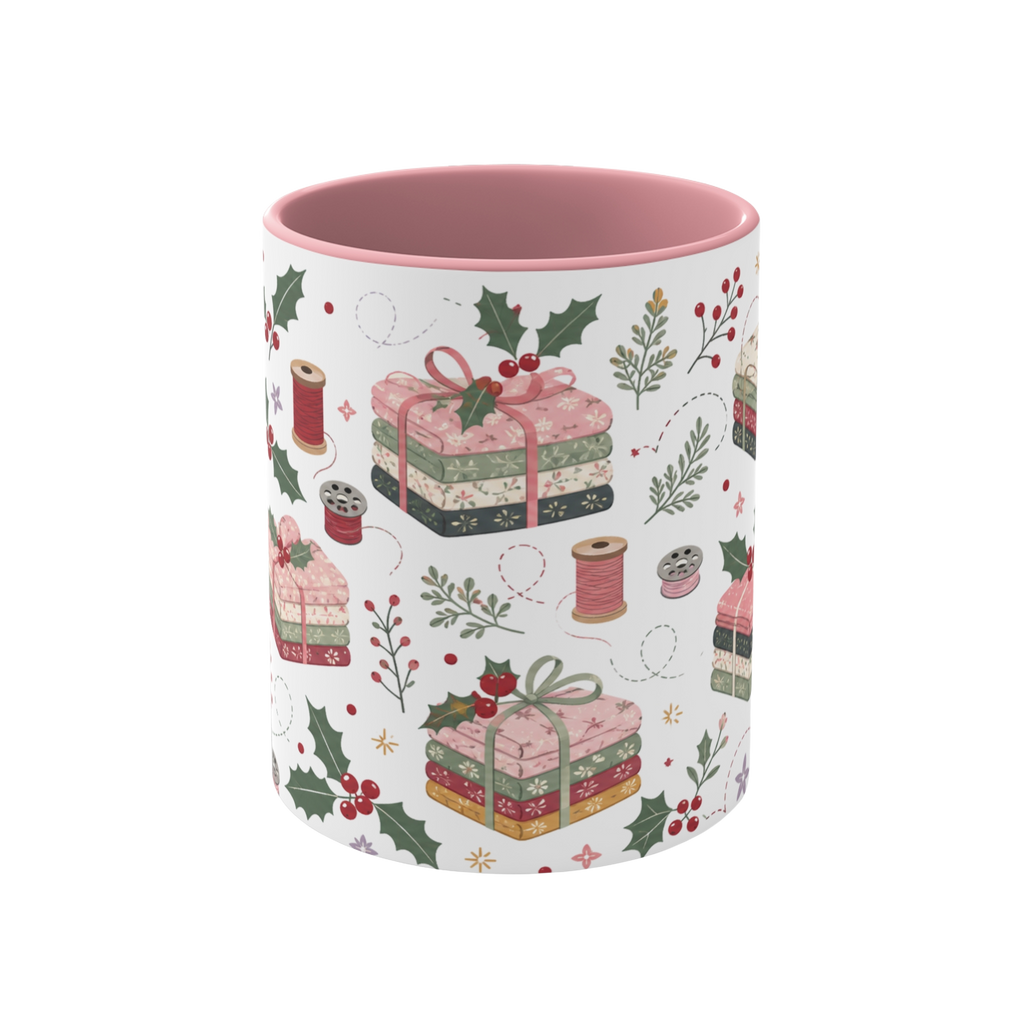 The front of a white ceramic mug with a pink interior, decorated with a repeating pattern of stacked fabrics, holly leaves, berries, and thread spools in soft pink, green, beige, and brown tones.