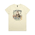 A pale butter yellow short-sleeve t-shirt with the words 'Cat Hair is Quilt Glitter' around an illustration of a cat sitting on a quilt surrounded by sewing accessories.