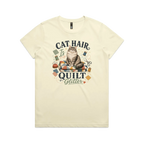 A pale butter yellow short-sleeve t-shirt with the words 'Cat Hair is Quilt Glitter' around an illustration of a cat sitting on a quilt surrounded by sewing accessories.