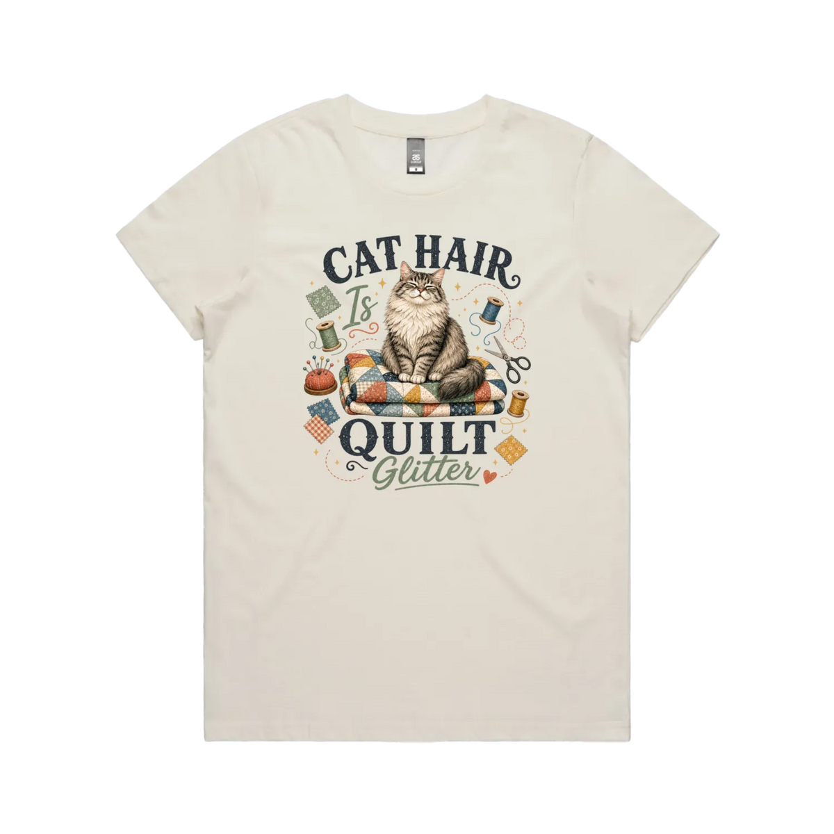 An off-white short-sleeve t-shirt with the words 'Cat Hair is Quilt Glitter' around an illustration of a cat sitting on a quilt surrounded by sewing accessories.