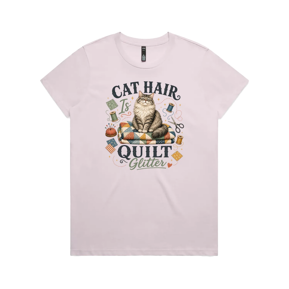 A pale mauve short-sleeve t-shirt with the words 'Cat Hair is Quilt Glitter' around an illustration of a cat sitting on a quilt surrounded by sewing accessories.