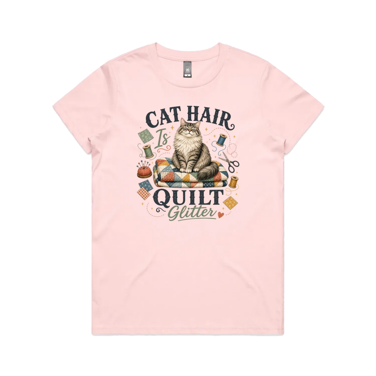 A pale pink short-sleeve t-shirt with the words 'Cat Hair is Quilt Glitter' around an illustration of a cat sitting on a quilt surrounded by sewing accessories.