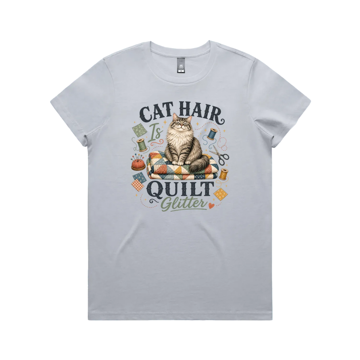 A powder blue short-sleeve t-shirt with the words 'Cat Hair is Quilt Glitter' around an illustration of a cat sitting on a quilt surrounded by sewing accessories.
