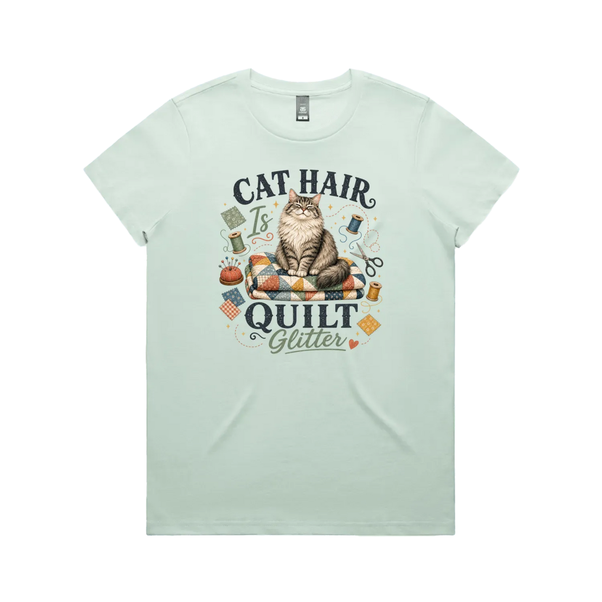 A pale mint green short-sleeve t-shirt with the words 'Cat Hair is Quilt Glitter' around an illustration of a cat sitting on a quilt surrounded by sewing accessories.
