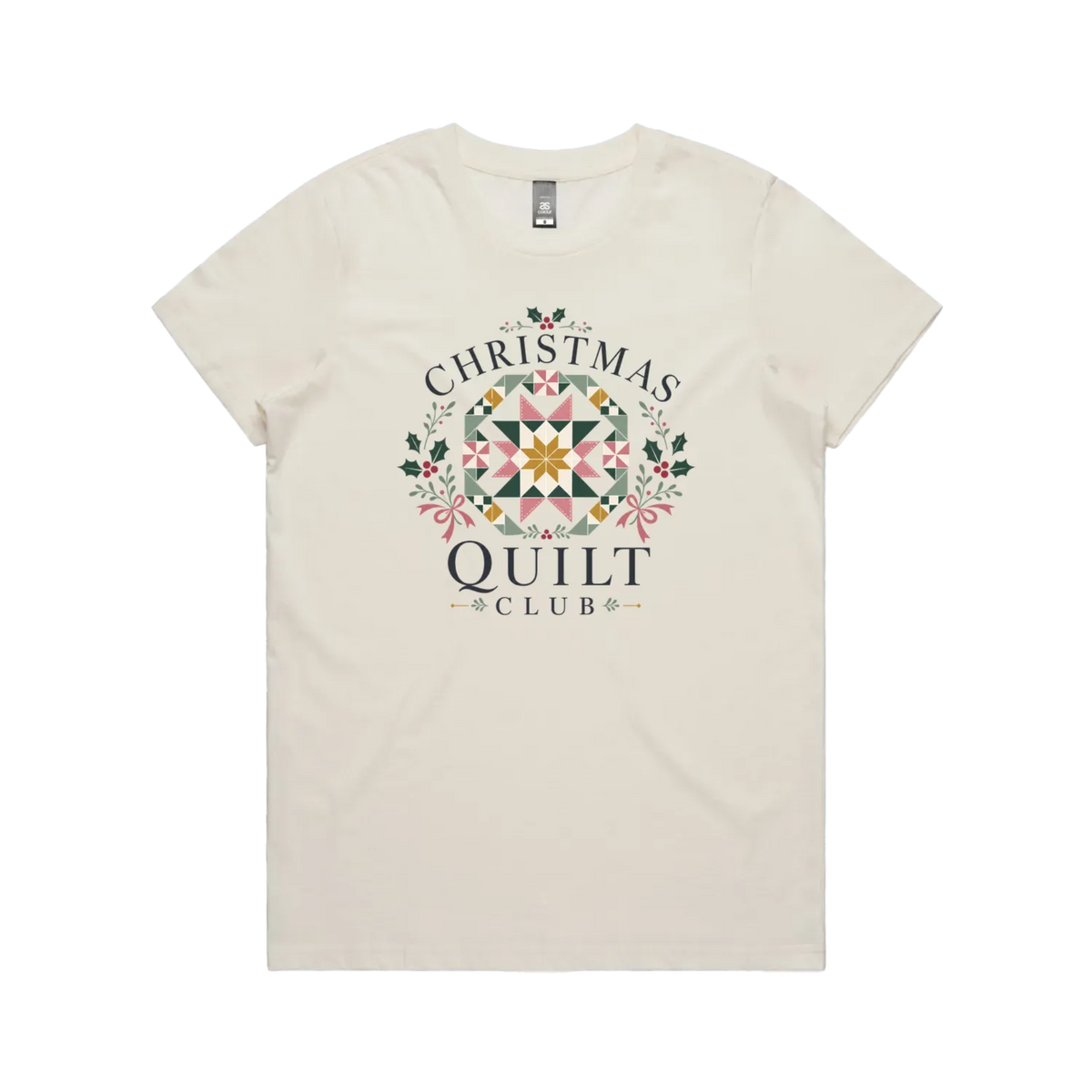 An off-white short-sleeve crewneck t-shirt featuring a 'Christmas Quilt Club' graphic on the front. The graphic includes a colorful geometric quilt pattern in the center, surrounded by green holly leaves and pink bows, with the words 'CHRISTMAS QUILT CLUB' printed in dark gray.