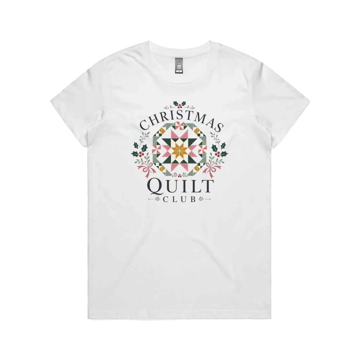 A white short-sleeve crewneck t-shirt featuring a 'Christmas Quilt Club' graphic on the front. The graphic includes a colorful geometric quilt pattern in the center, surrounded by green holly leaves and pink bows, with the words 'CHRISTMAS QUILT CLUB' printed in dark gray.