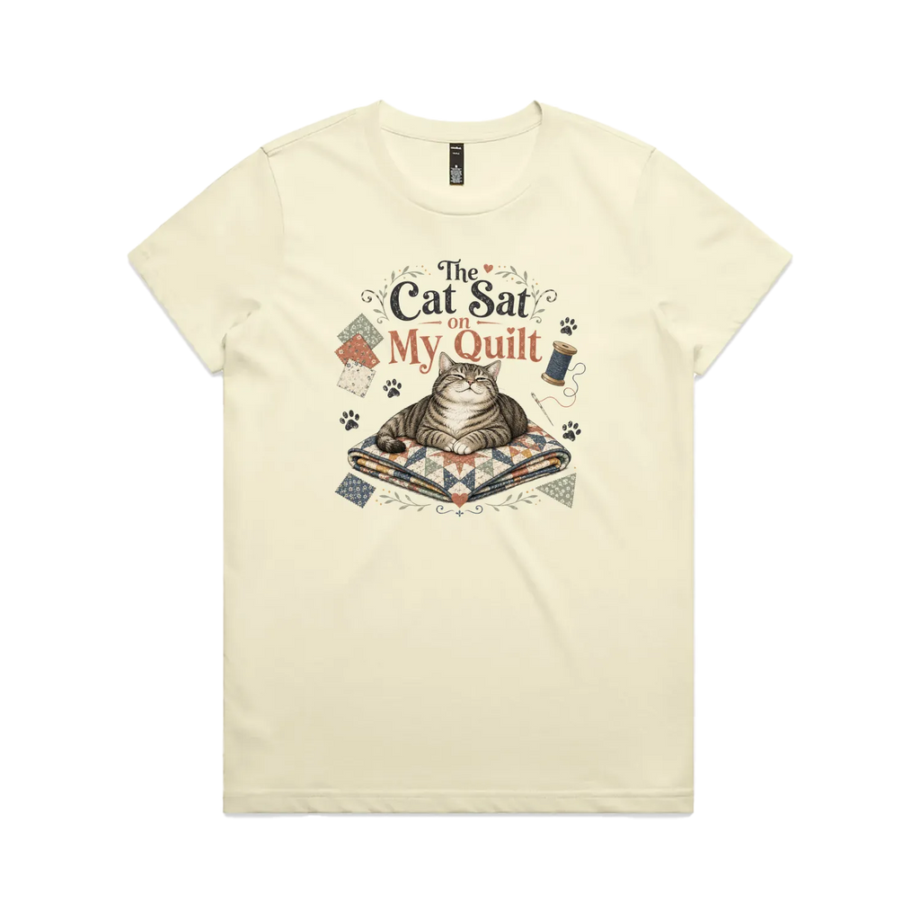 A pale butter yellow short-sleeve t-shirt with an illustration of a cat sitting on a quilt surrounded by sewing accessories and the words 'The Cat Sat on My Quilt'.