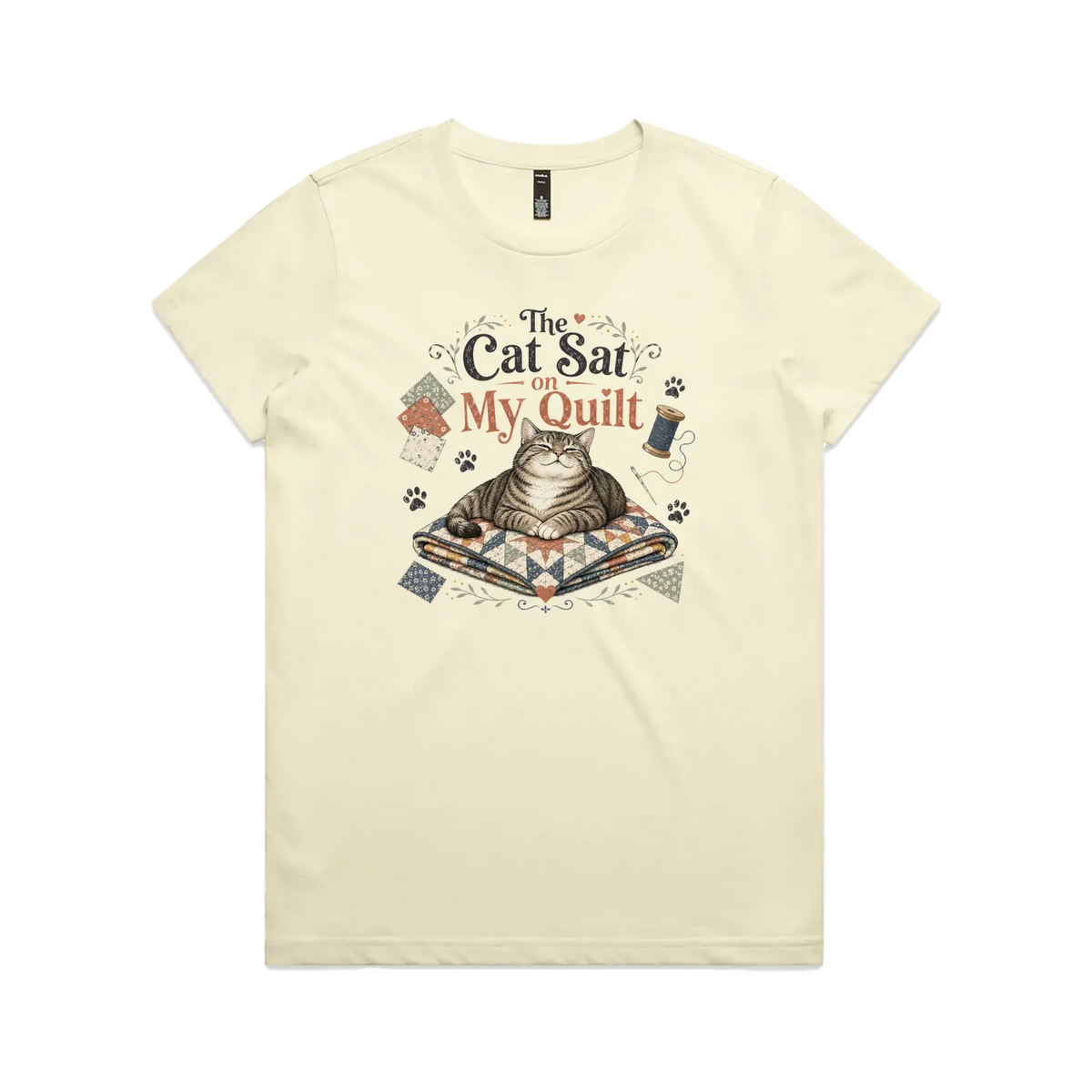 A pale butter yellow short-sleeve t-shirt with an illustration of a cat sitting on a quilt surrounded by sewing accessories and the words 'The Cat Sat on My Quilt'.