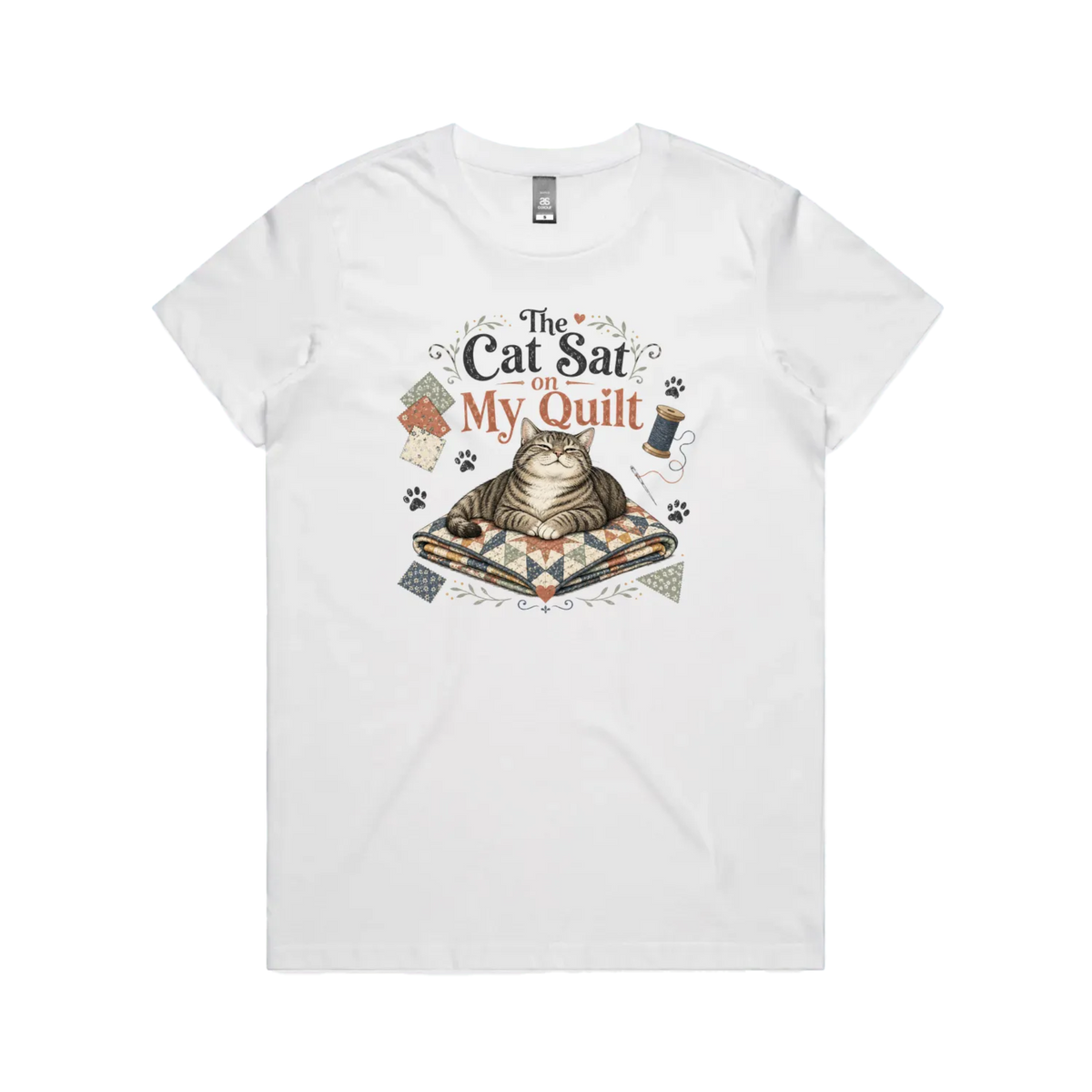 A white short-sleeve t-shirt with an illustration of a cat sitting on a quilt surrounded by sewing accessories and the words 'The Cat Sat on My Quilt'.