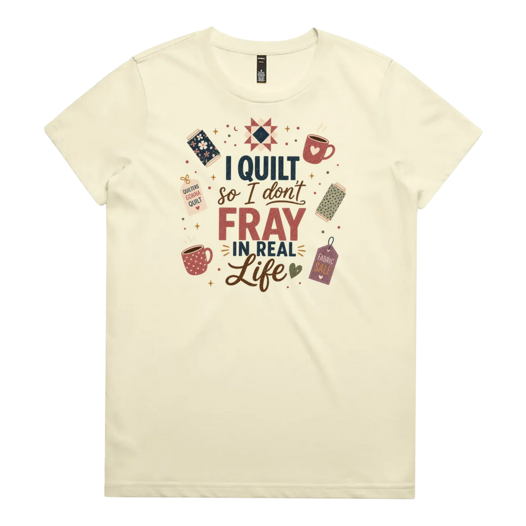 A pale butter yellow short-sleeve crewneck t-shirt featuring a colorful graphic print on the front with quilting-themed illustrations and the text 'I Quilt So I Don't Fray in Real Life'.