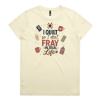 A pale butter yellow short-sleeve crewneck t-shirt featuring a colorful graphic print on the front with quilting-themed illustrations and the text 'I Quilt So I Don't Fray in Real Life'.