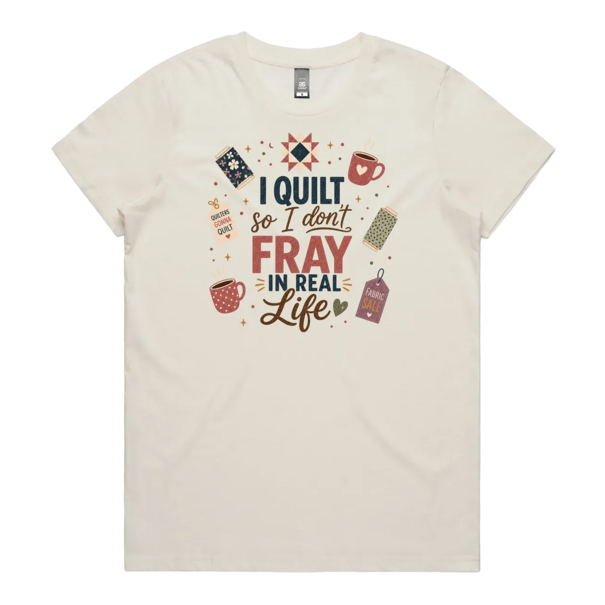 An off-white short-sleeve crewneck t-shirt featuring a colorful graphic print on the front with quilting-themed illustrations and the text 'I Quilt So I Don't Fray in Real Life'.