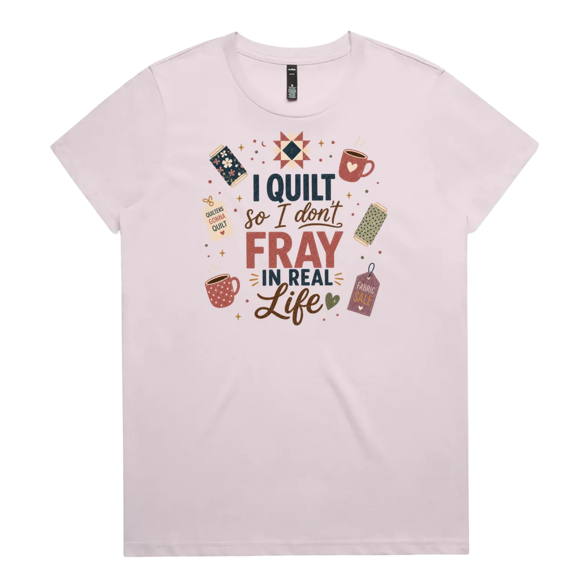 A pale mauve short-sleeve crewneck t-shirt featuring a colorful graphic print on the front with quilting-themed illustrations and the text 'I Quilt So I Don't Fray in Real Life'.