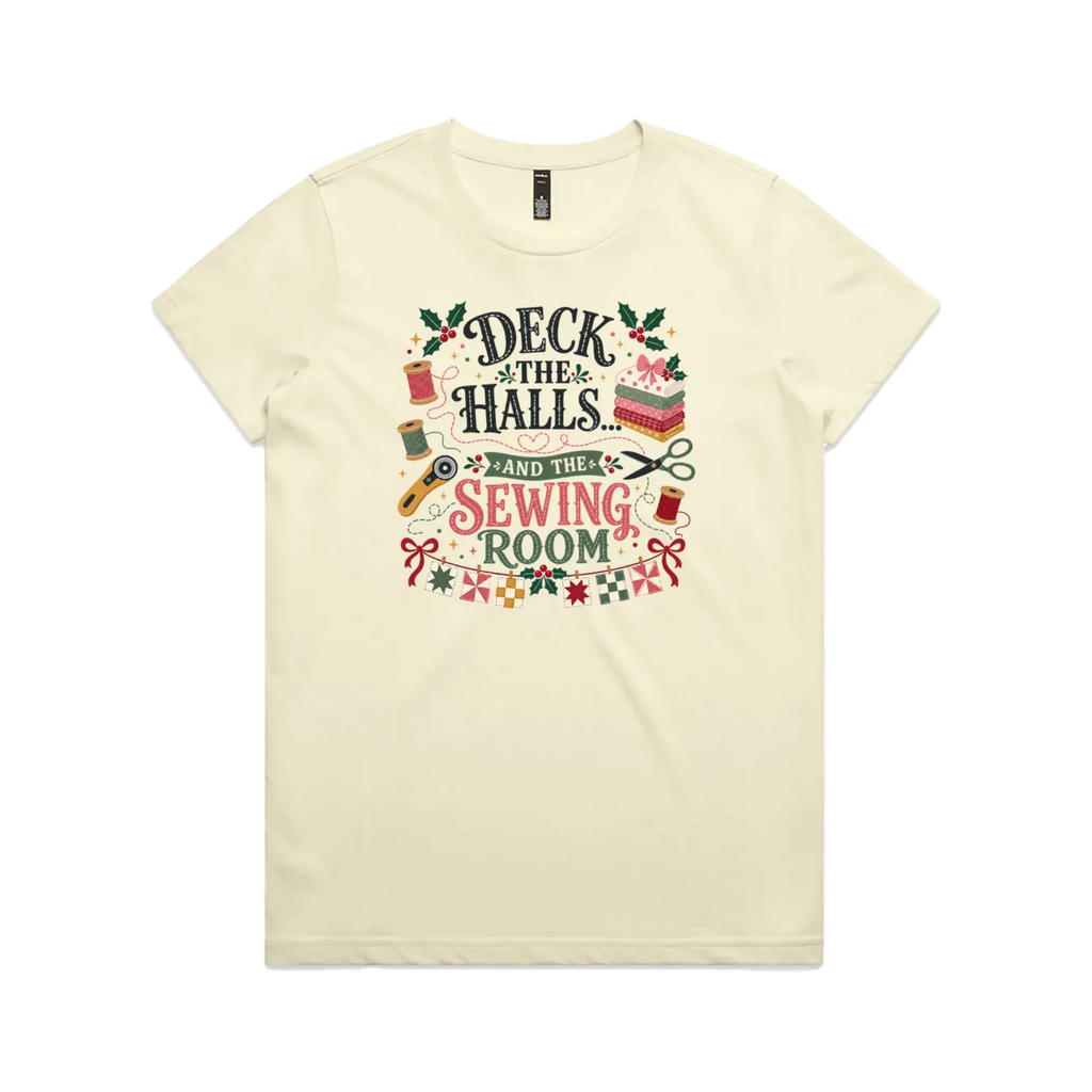A pale butter yellow short-sleeve crewneck t-shirt featuring a colorful graphic print on the front with sewing-themed illustrations and the text 'Deck the Halls and the Sewing Room'.
