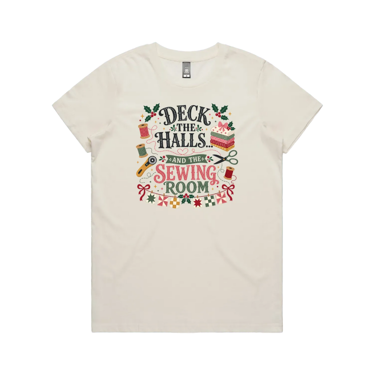An off-white short-sleeve crewneck t-shirt featuring a colorful graphic print on the front with sewing-themed illustrations and the text 'Deck the Halls and the Sewing Room'.