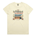 A pale butter yellow crewneck short-sleeve t-shirt with the words 'Fabric Acquisition Specialist' above a stack of fabric bolts, a measuring tape, thread spool and scissors.