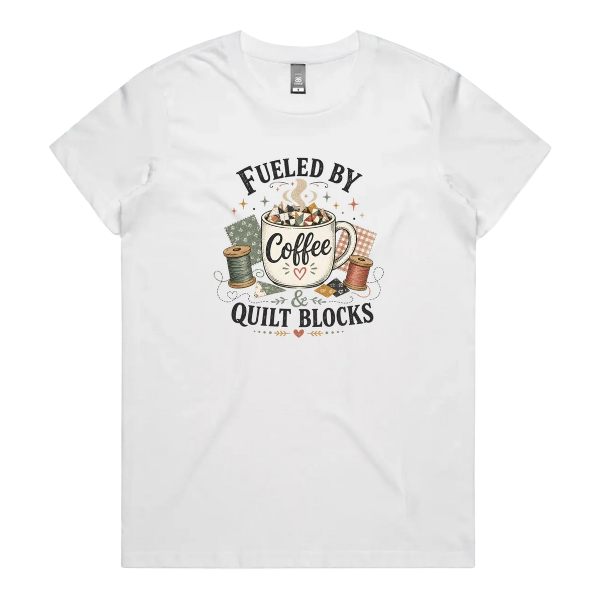 A white short-sleeve t-shirt with a vintage-style graphic on the front that reads 'Fueled by Coffee & Quilt Blocks' around an illustration of a coffee mug, quilting thread spools, and fabric.