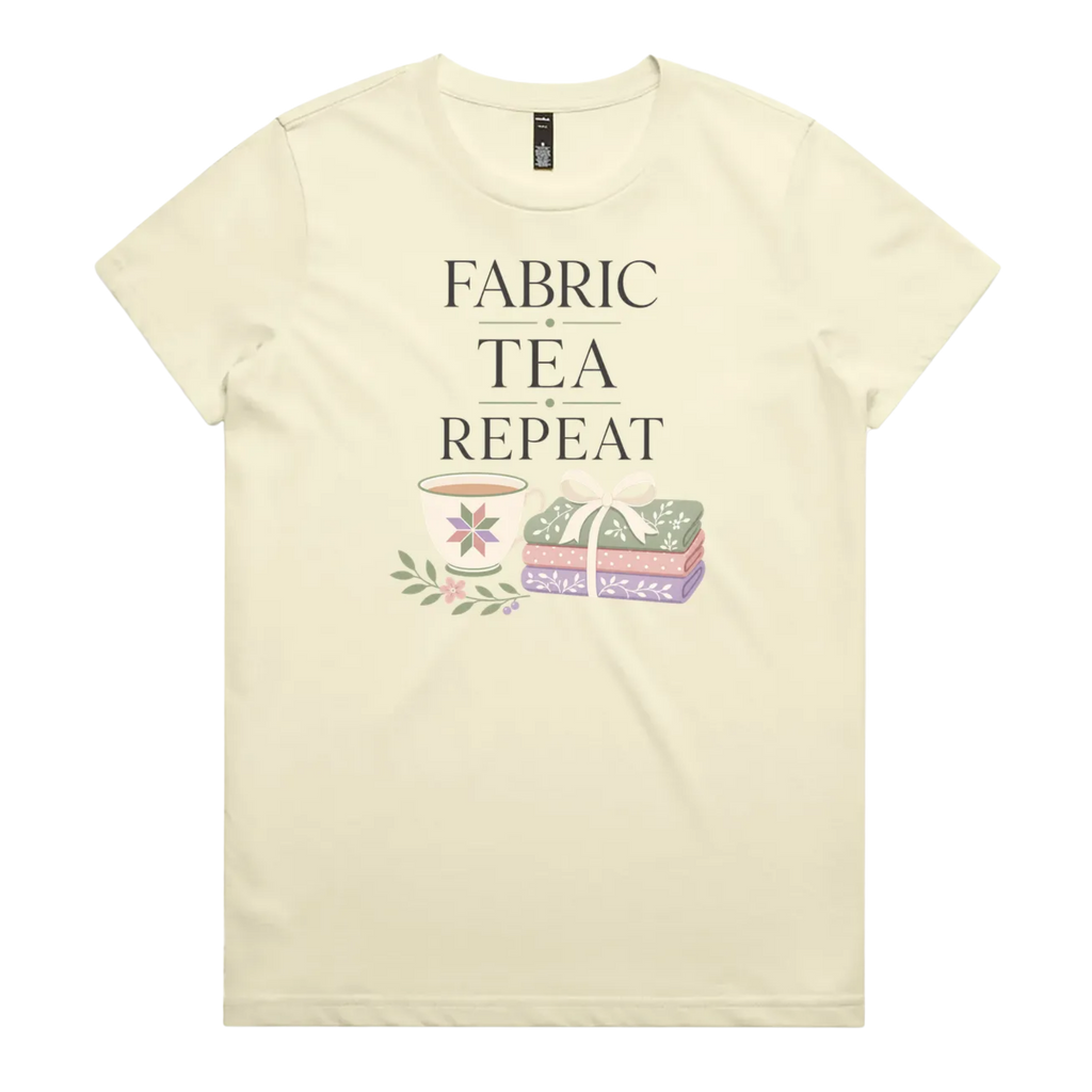 A pale butter yellow short-sleeve crewneck t-shirt featuring a graphic print that reads 'FABRIC, TEA, REPEAT' above an illustration of a teacup, floral details, and patterned fabric stack.
