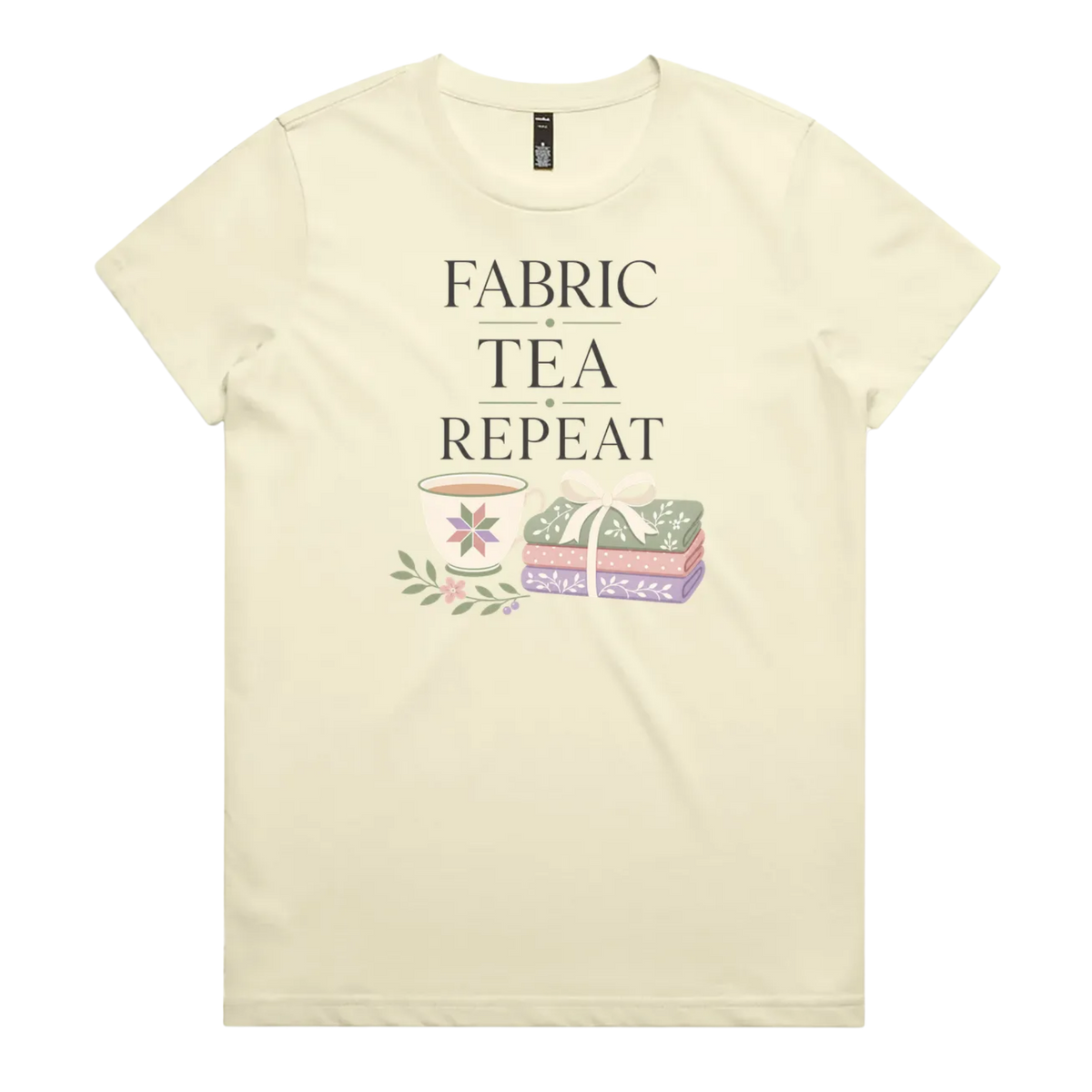 A pale butter yellow short-sleeve crewneck t-shirt featuring a graphic print that reads 'FABRIC, TEA, REPEAT' above an illustration of a teacup, floral details, and patterned fabric stack.