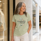 A woman with long grey hair stands outside a boutique in a shopping mall wearing a pistachio green t-shirt with the words 'Geometry & Thread' surrounded by illustrations of patchwork triangles.