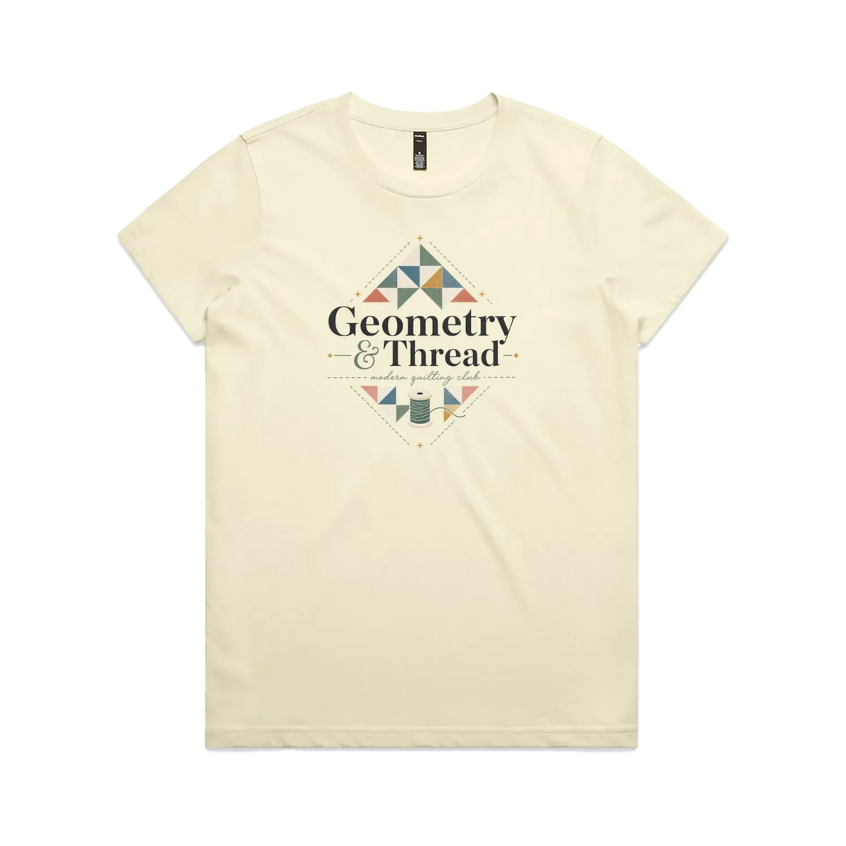 A pale butter yellow short-sleeve crewneck graphic t-shirt featuring the words 'Geometry & Thread, Modern Quilting Club' surrounded by patchwork triangles and a spool of thread.