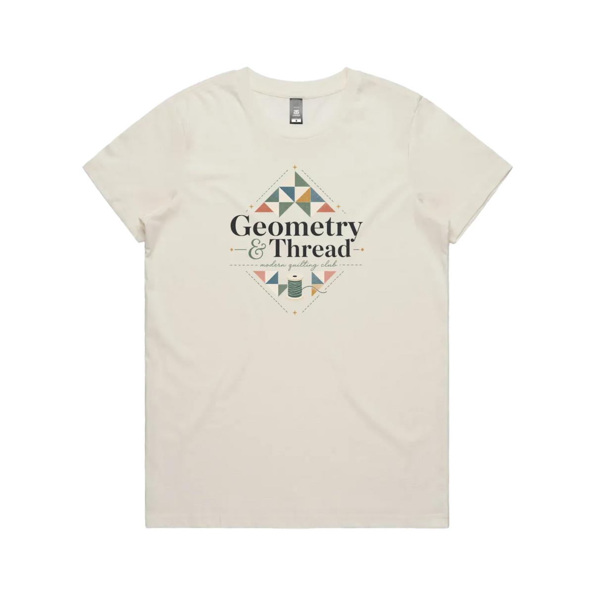 A pale cream short-sleeve crewneck graphic t-shirt featuring the words 'Geometry & Thread, Modern Quilting Club' surrounded by patchwork triangles and a spool of thread.
