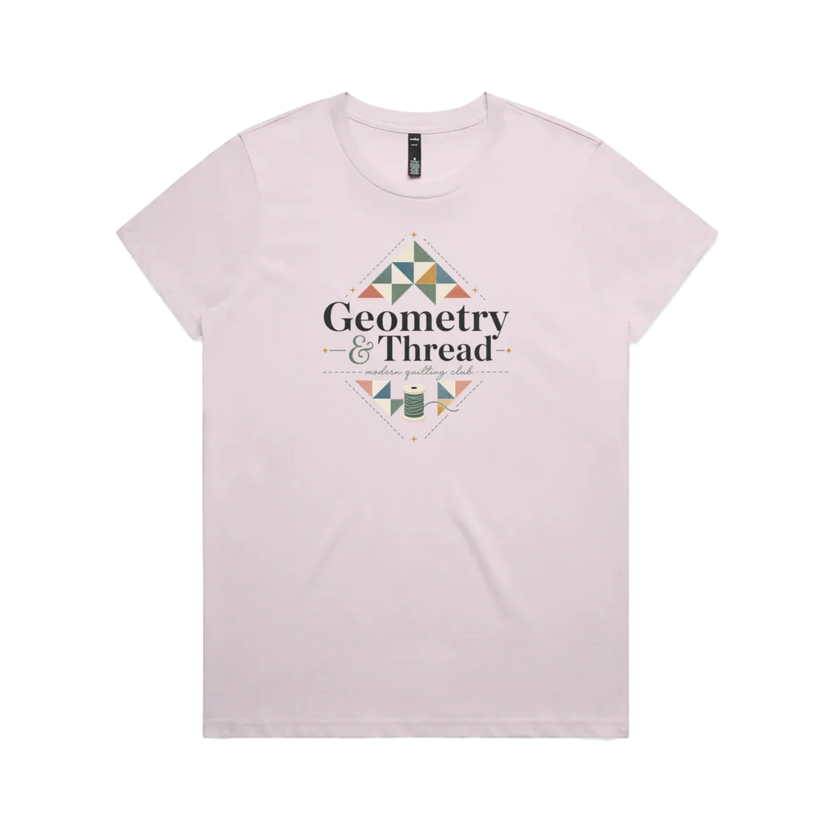 A pale mauve short-sleeve crewneck graphic t-shirt featuring the words 'Geometry & Thread, Modern Quilting Club' surrounded by patchwork triangles and a spool of thread.