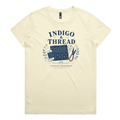 A pale butter yellow short-sleeve crewneck t-shirt featuring a navy blue and multicolor graphic on the front that reads 'INDIGO & THREAD' with a spool of thread, sashiko fabric swatch, scissors, and 'SASHIKO WORKSHOP' printed below.