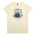 A pale butter yellow short-sleeve crewneck t-shirt featuring a navy blue and multicolor graphic on the front that reads 'INDIGO & THREAD' with a spool of thread, sashiko fabric swatch, scissors, and 'SASHIKO WORKSHOP' printed below.