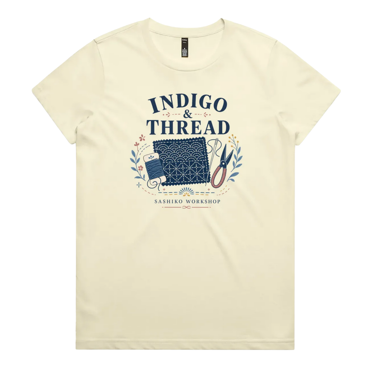 A pale butter yellow short-sleeve crewneck t-shirt featuring a navy blue and multicolor graphic on the front that reads 'INDIGO & THREAD' with a spool of thread, sashiko fabric swatch, scissors, and 'SASHIKO WORKSHOP' printed below.