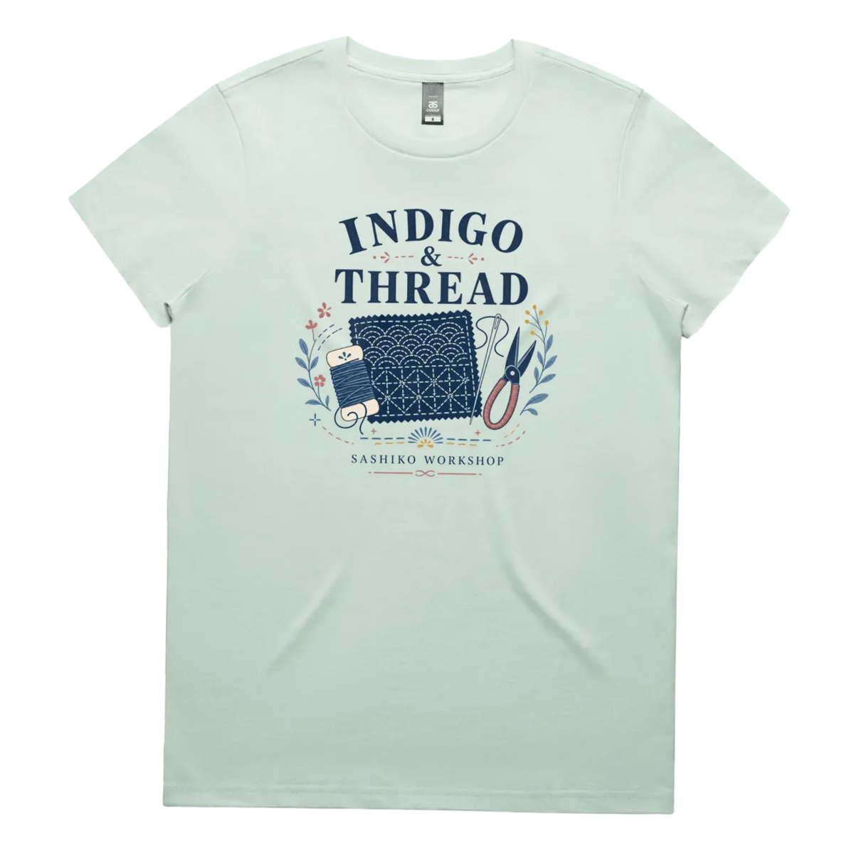 A pale seafoam green short-sleeve crewneck t-shirt featuring a navy blue and multicolor graphic on the front that reads 'INDIGO & THREAD' with a spool of thread, sashiko fabric swatch, scissors, and 'SASHIKO WORKSHOP' printed below.