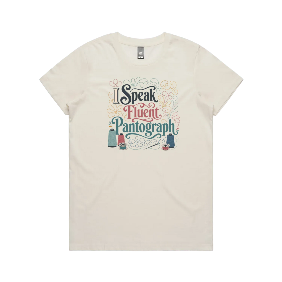 An off-white graphic short-sleeve t-shirt with the words 'I Speak Fluent Pantrograph' surrounded by thread spools, bobbins, a needle and swirling stitche lines in multi colours.