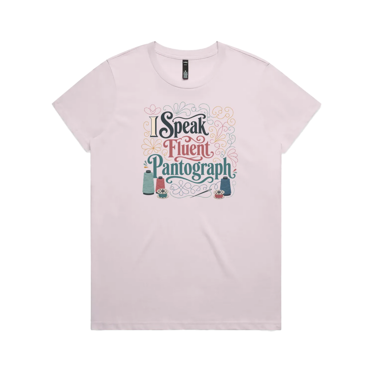 A pale mauve graphic short-sleeve t-shirt with the words 'I Speak Fluent Pantrograph' surrounded by thread spools, bobbins, a needle and swirling stitche lines in multi colours.