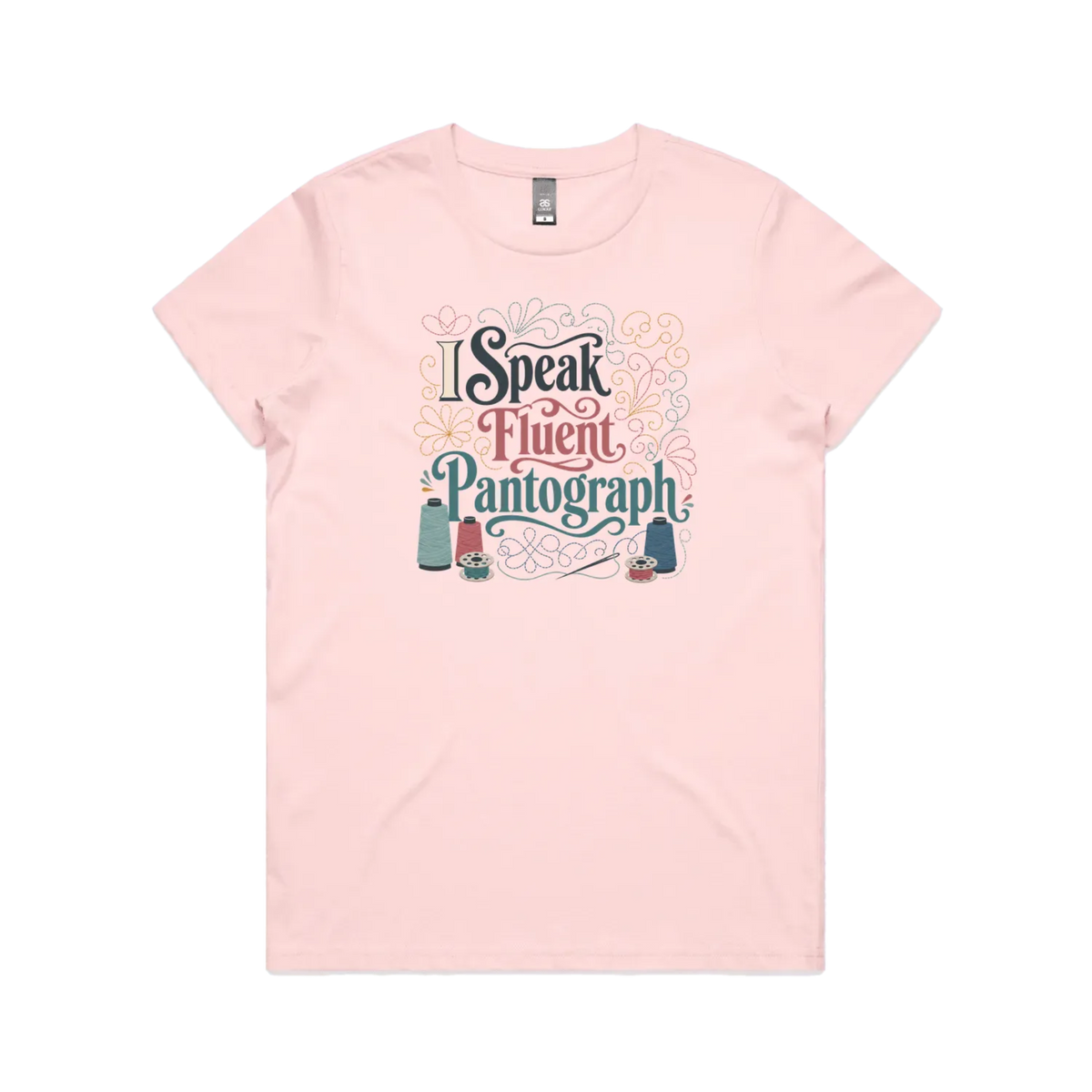 A pale pink graphic short-sleeve t-shirt with the words 'I Speak Fluent Pantrograph' surrounded by thread spools, bobbins, a needle and swirling stitche lines in multi colours.