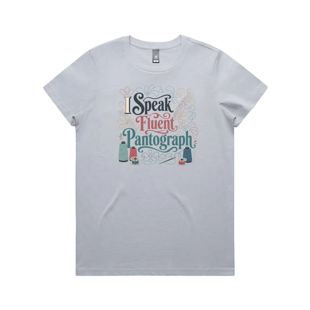 A powder blue graphic short-sleeve t-shirt with the words 'I Speak Fluent Pantrograph' surrounded by thread spools, bobbins, a needle and swirling stitche lines in multi colours.