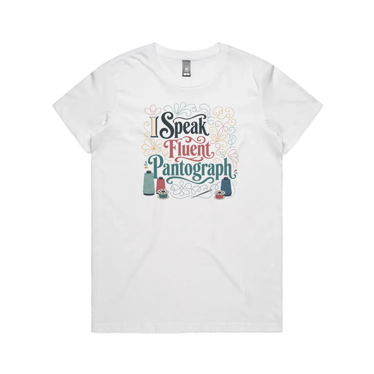 A white graphic short-sleeve t-shirt with the words 'I Speak Fluent Pantrograph' surrounded by thread spools, bobbins, a needle and swirling stitche lines in multi colours.