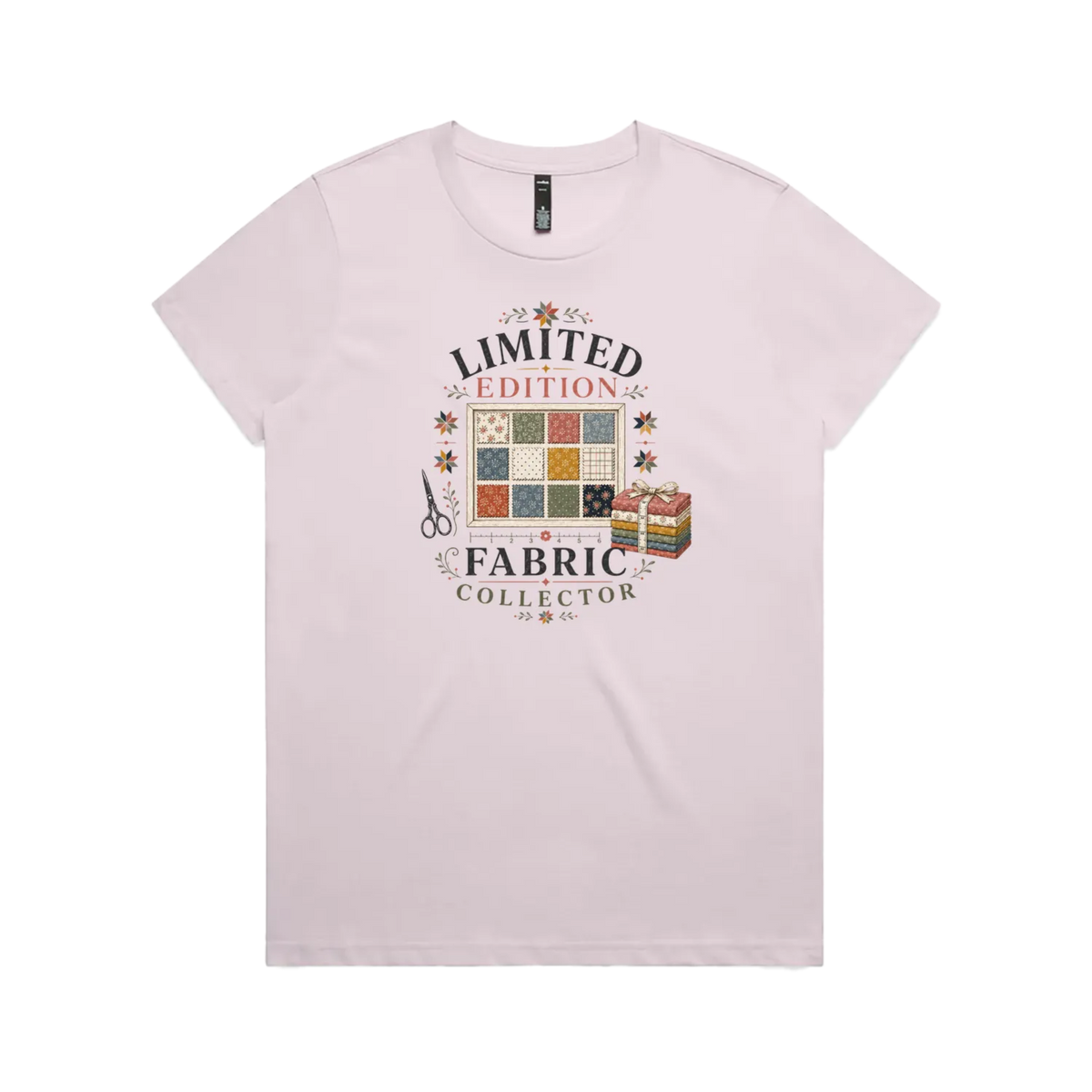 A pale mauve short-sleeve crewneck t-shirt featuring the text 'Limited Edition Fabric Collector' surround a fabric swatch board, a tied bundle of fabric and scissors.